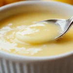 Sauce beurre blanc citronnée onctueuse dans un bol blanc, cuillère argentée, citrons jaunes en arrière-plan, ciboulette fraîche, SavoryGlobe.