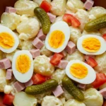 Salade piemontaise traditionnelle dans un bol coloré, garnie de tomates, pommes de terre, jambon et sauce crémeuse, parfaite pour un repas authentique.